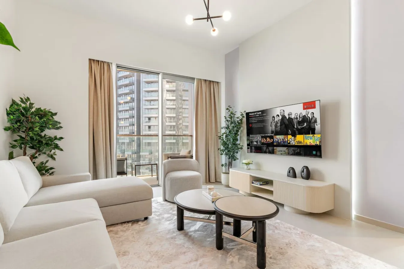 A bright living room with light seating, a television, and a large window.