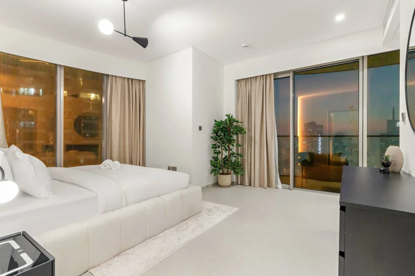 A bright bedroom with a large bed beside floor-to-ceiling windows.