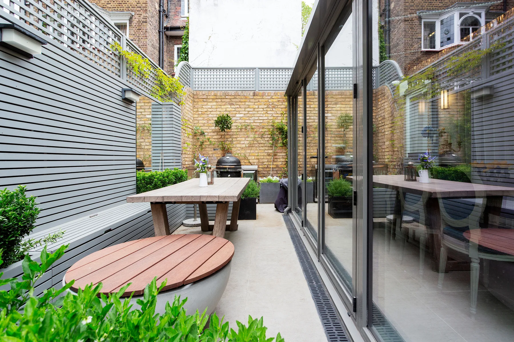 A small outdoor patio with a dining table, benches, and glass doors.