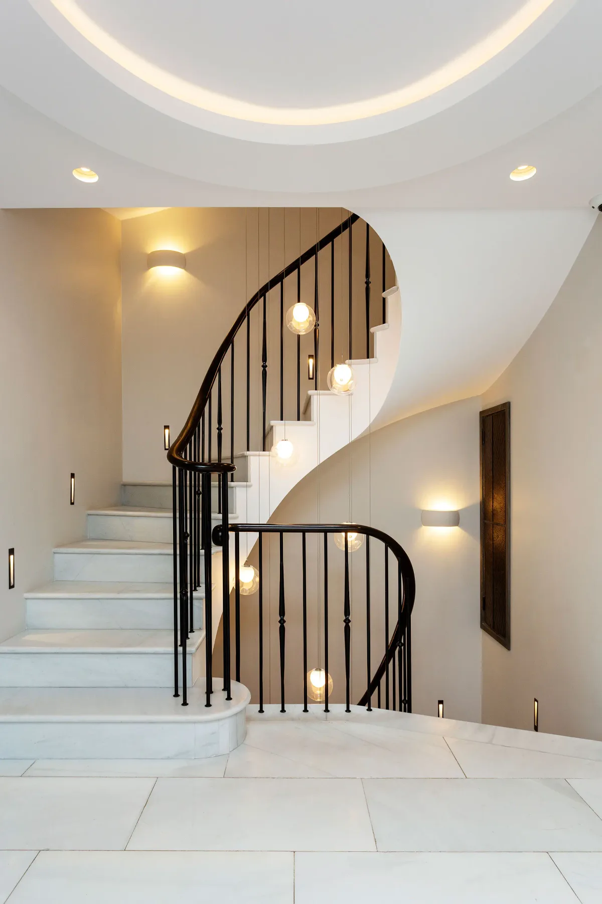 Una escalera curva con barandales oscuros sube por un interior luminoso.