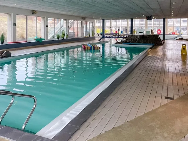 An indoor swimming pool with large windows and a tiled deck.