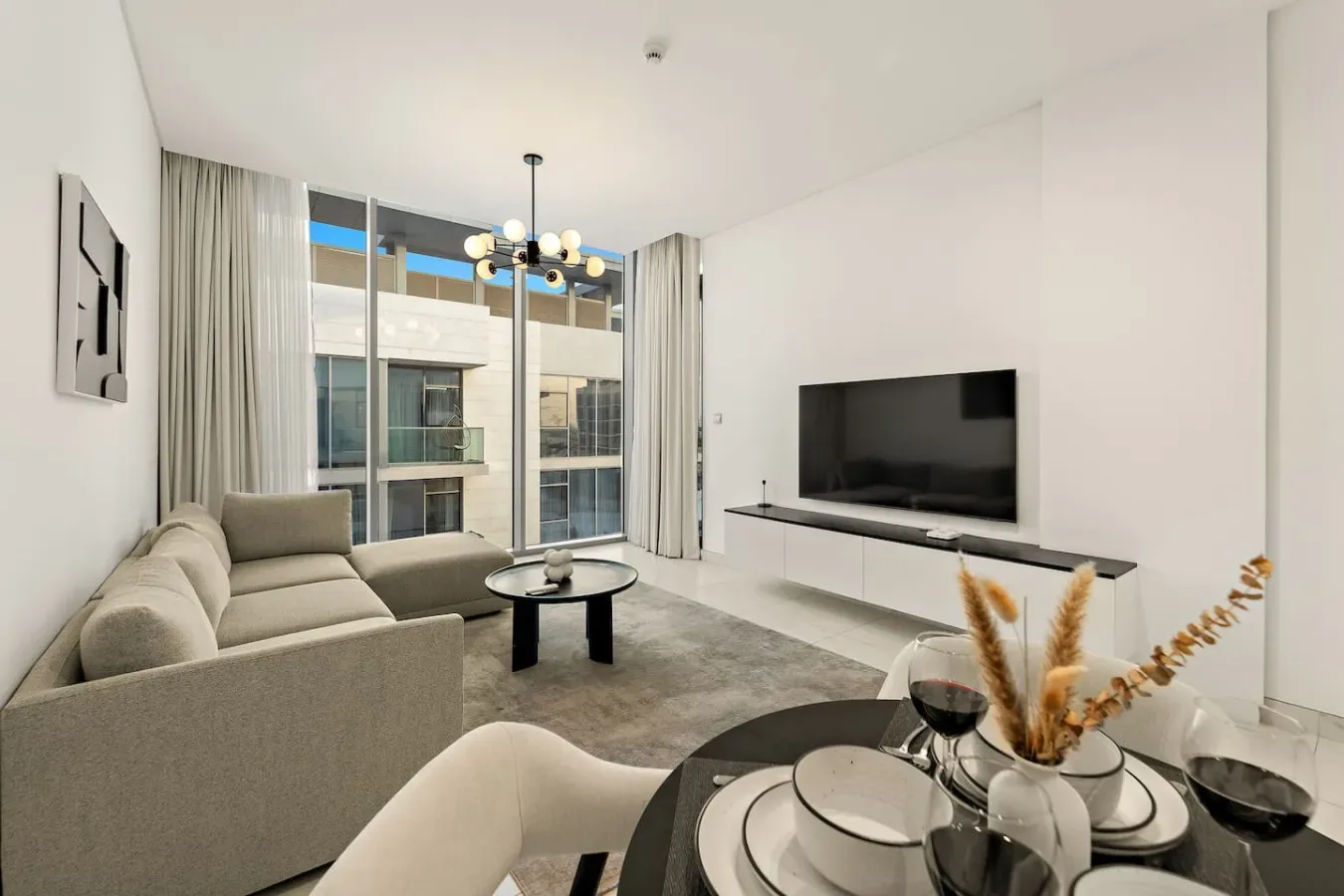 A bright living room with seating, a television, and floor-to-ceiling windows.