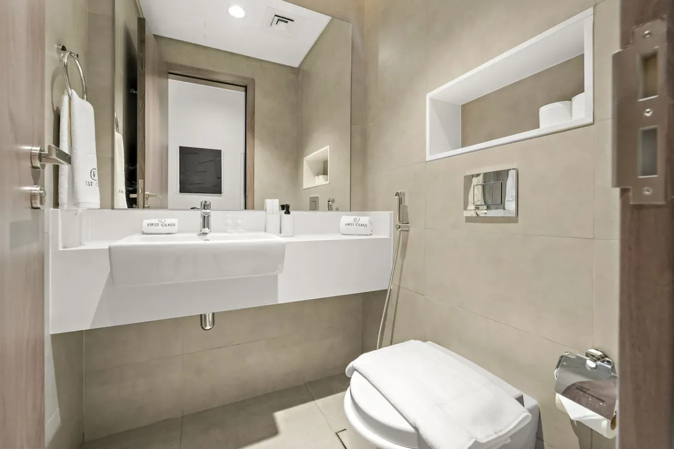 A tiled bathroom with a wall-mounted sink, mirror, and shower fixtures.