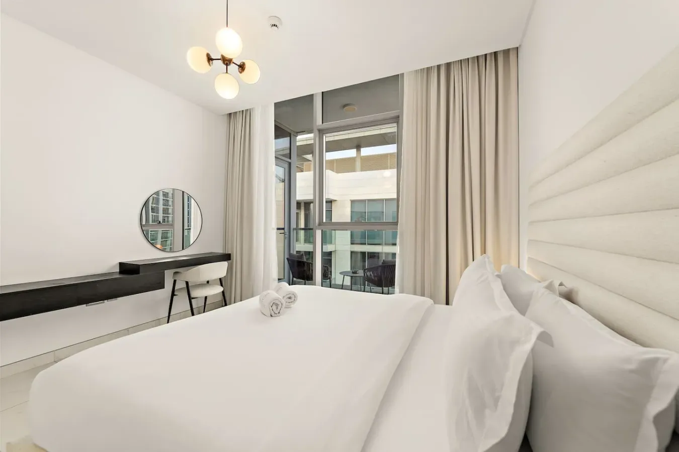 A bright bedroom with a large bed, a desk, and floor-length curtains.