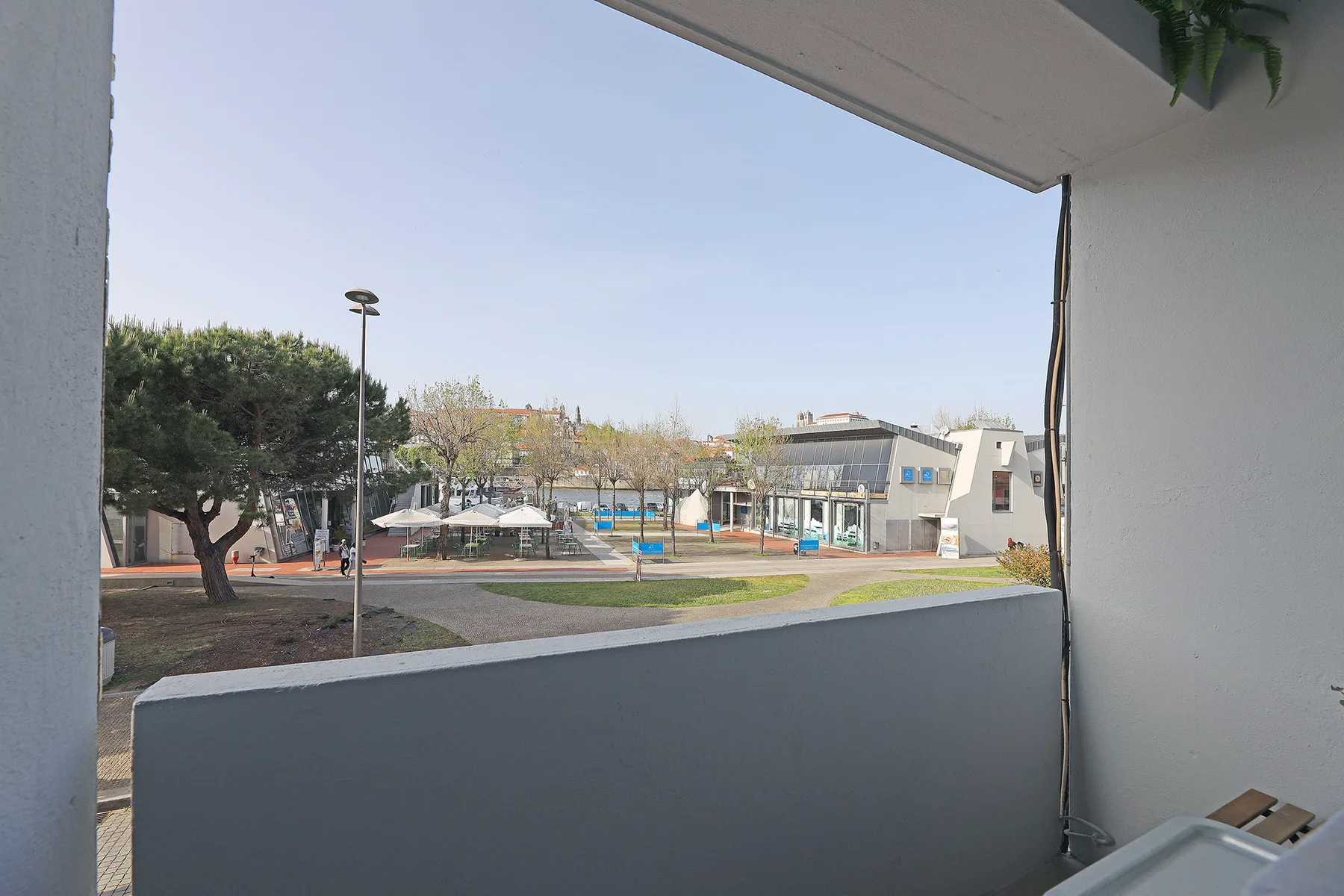 A balcony overlooks a landscaped public space with trees, paths, and low buildings.