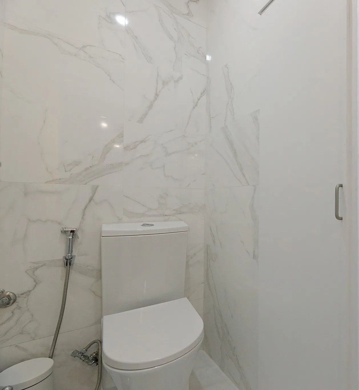 A bathroom with a toilet and light-colored tiled walls.