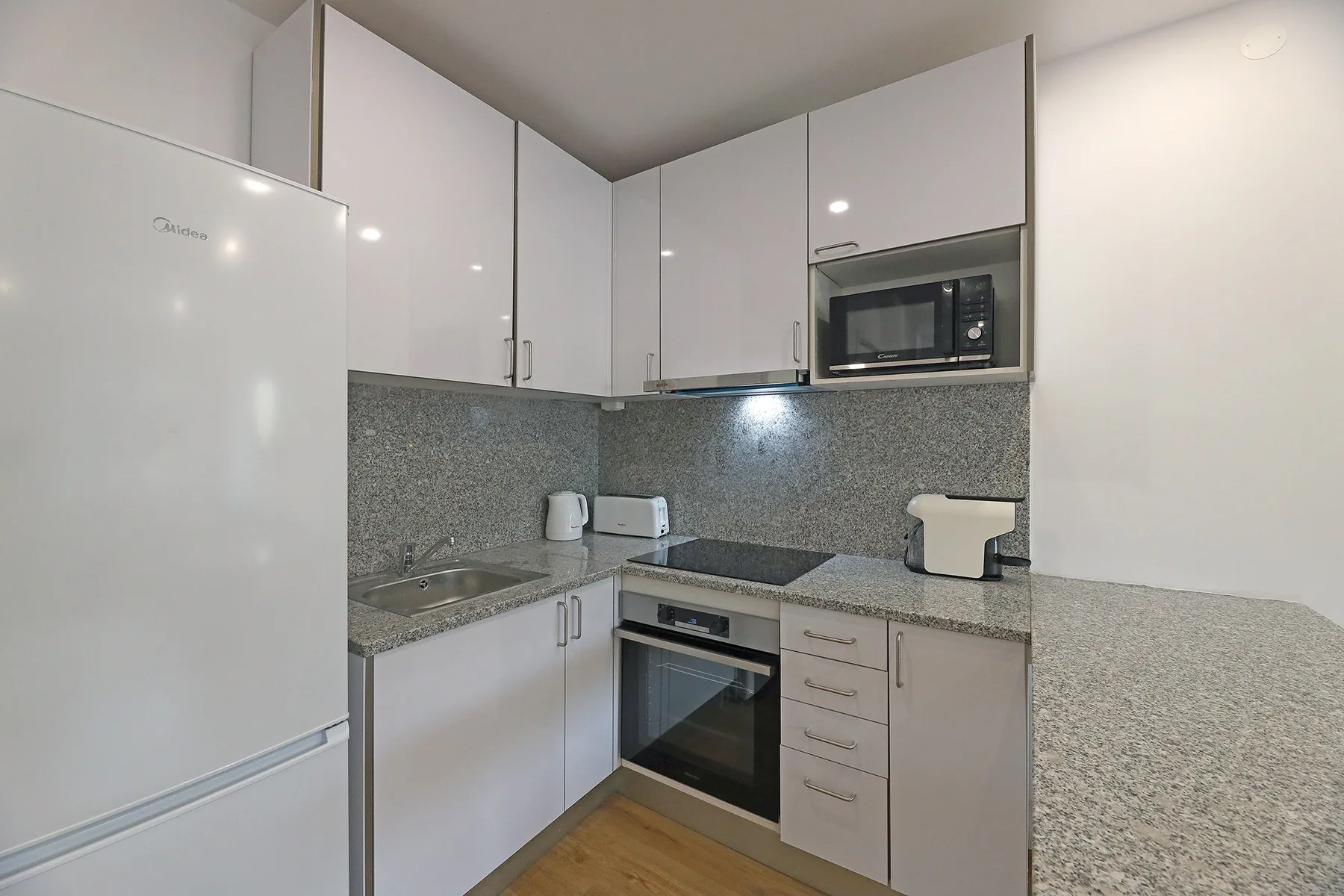 A compact kitchen with white cabinets, a refrigerator, and built-in appliances.