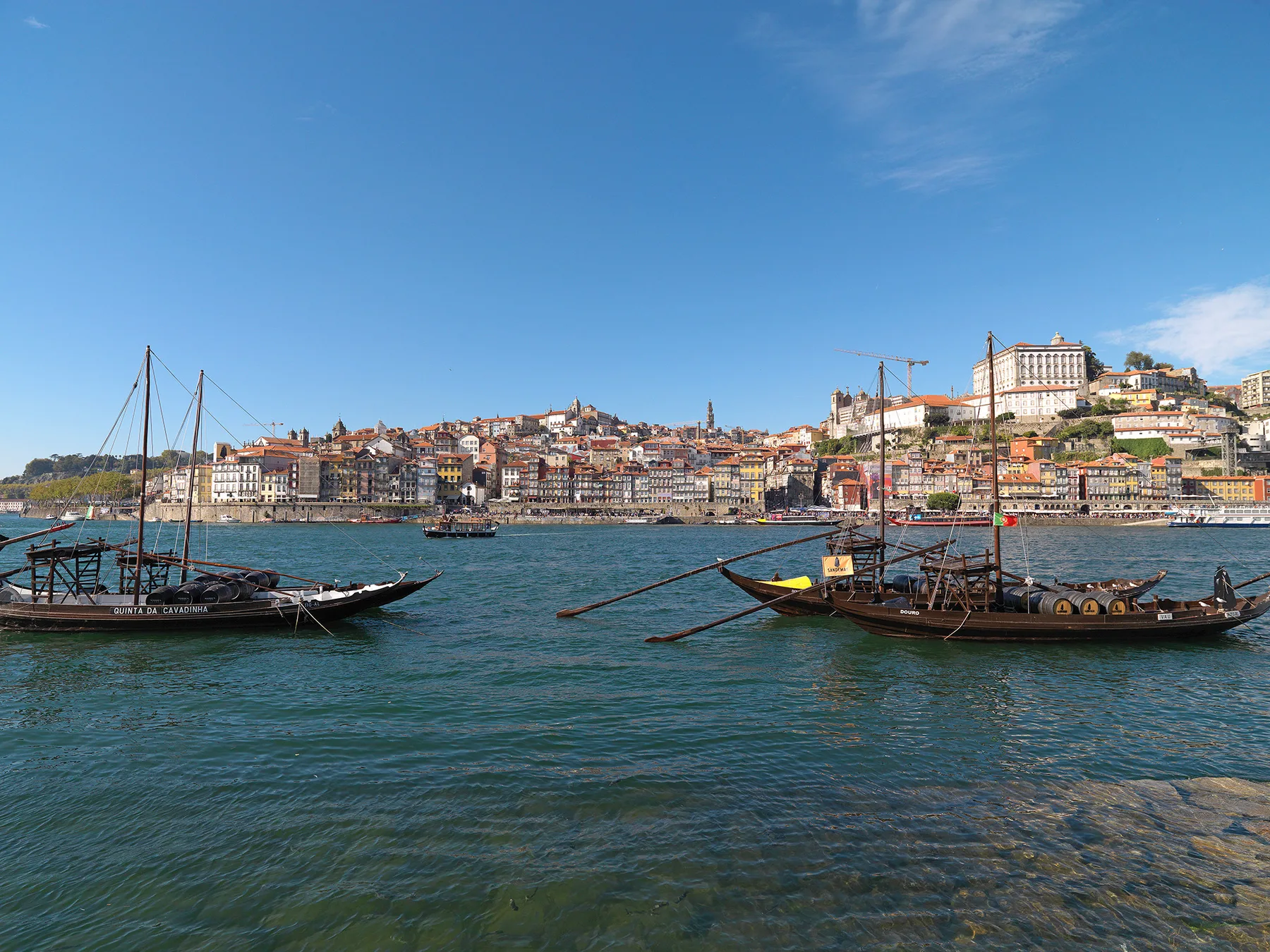 A riverfront cityscape with traditional boats on the water.