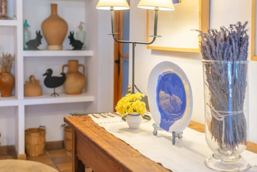 A decorated wooden table displays pottery, a floral arrangement, and a blue plate.