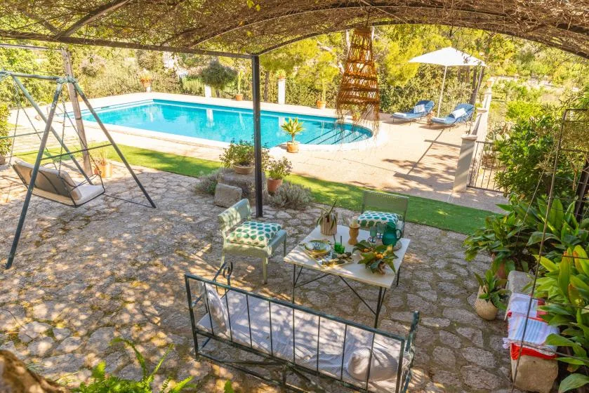 Un patio de piedra sombreado da a una piscina, con asientos al aire libre bajo un dosel frondoso.