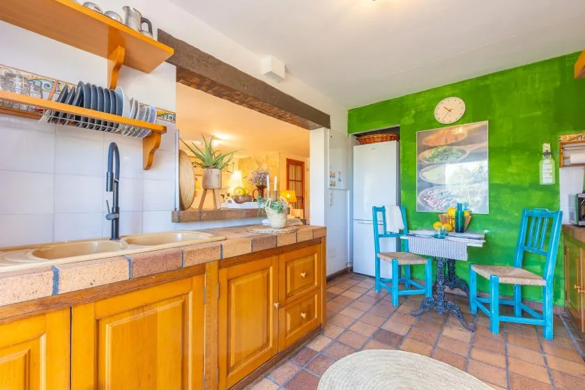 A kitchen with wooden cabinets and a dining table against a green wall.