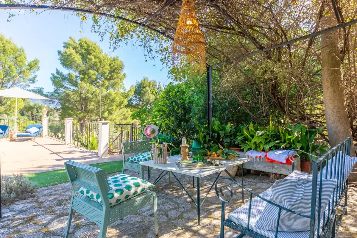An outdoor patio with seating and a table beneath leafy trees.
