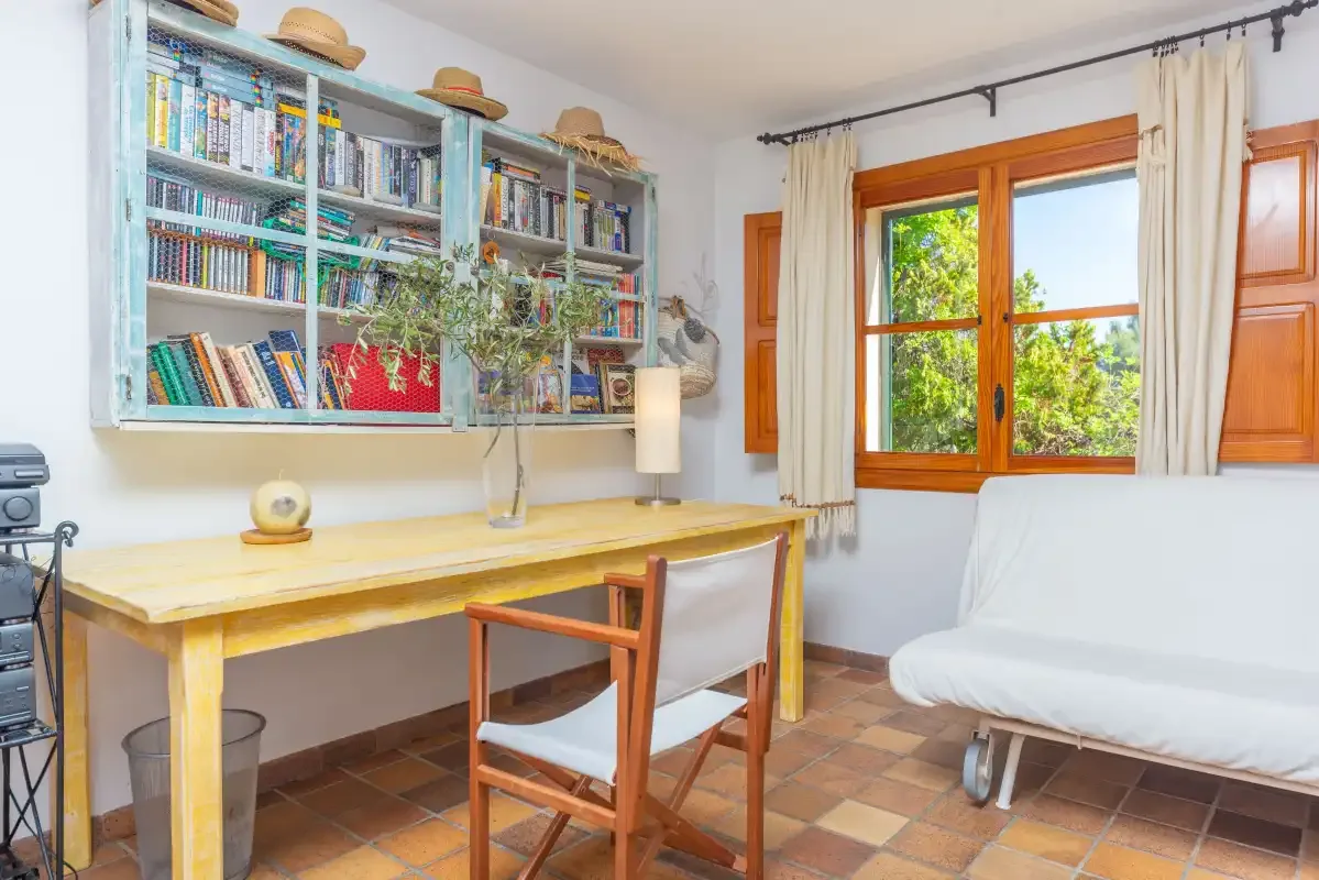 A bright room has a wooden desk, a chair, bookshelves, and a window.