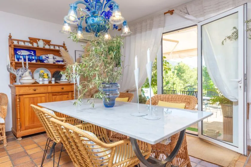 A dining area with a table, woven seating, and open glass doors to a leafy patio.