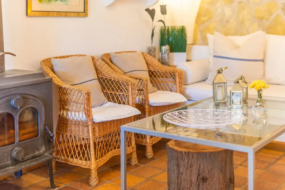 A living room with wicker seating, a glass coffee table, and a wood stove.