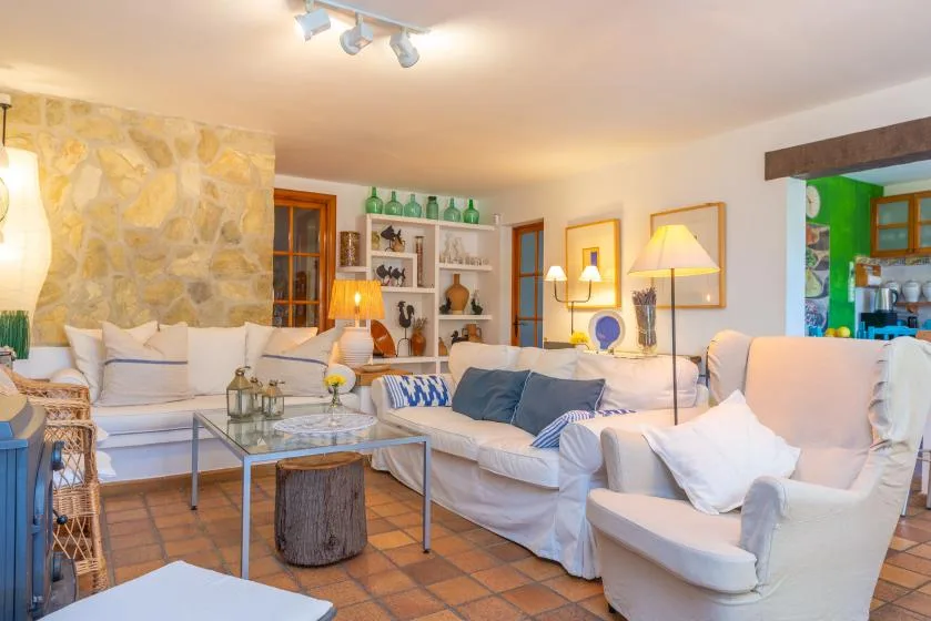 A bright living room with white seating, a glass coffee table, and a stone wall.