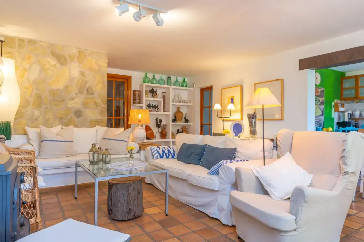 A living room with white seating, a glass coffee table, and a stone accent wall.
