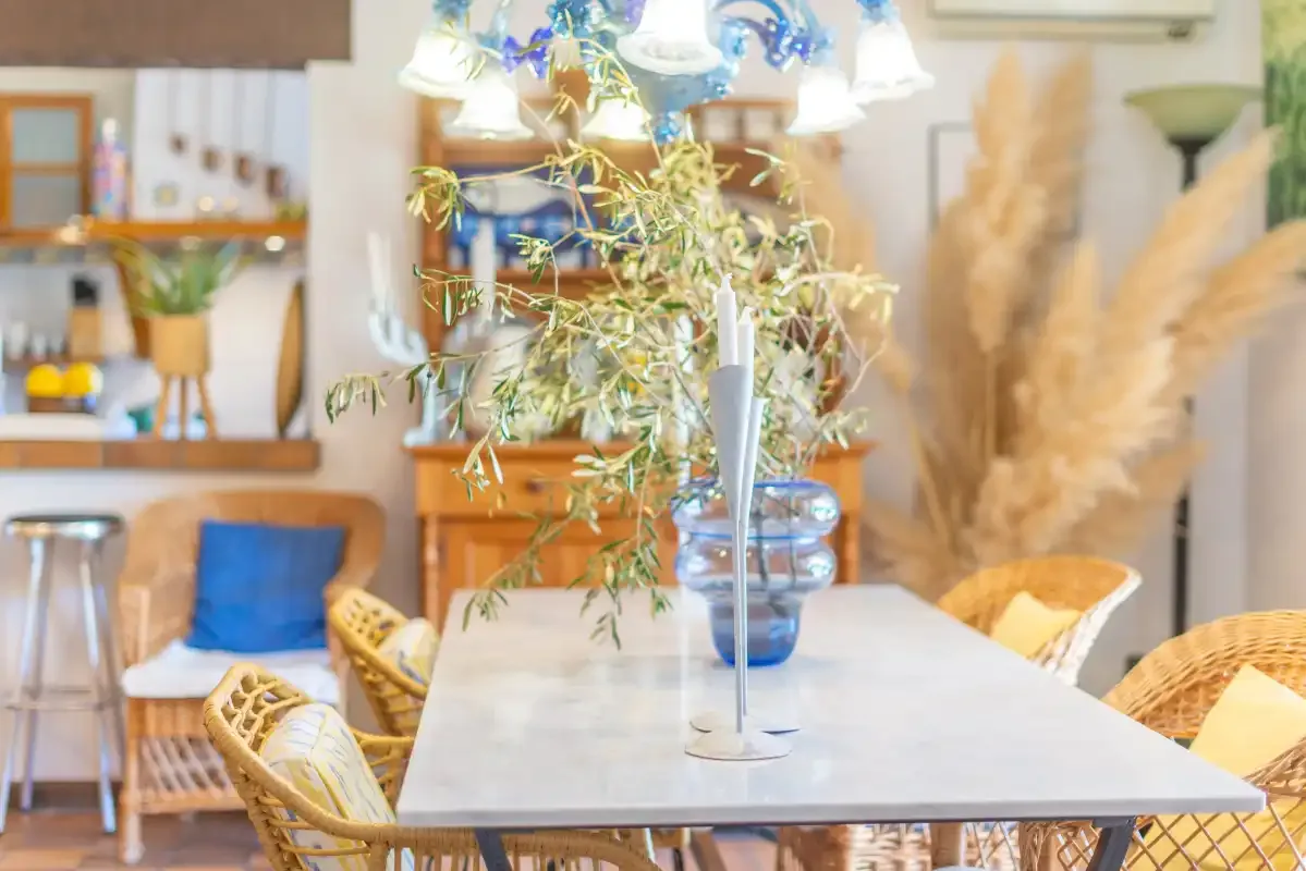 A dining area with a table, woven seating, and a leafy centerpiece.