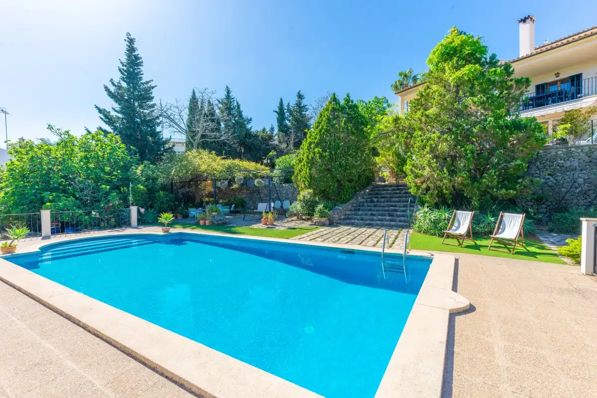 An outdoor swimming pool sits beside a garden with lounge chairs.