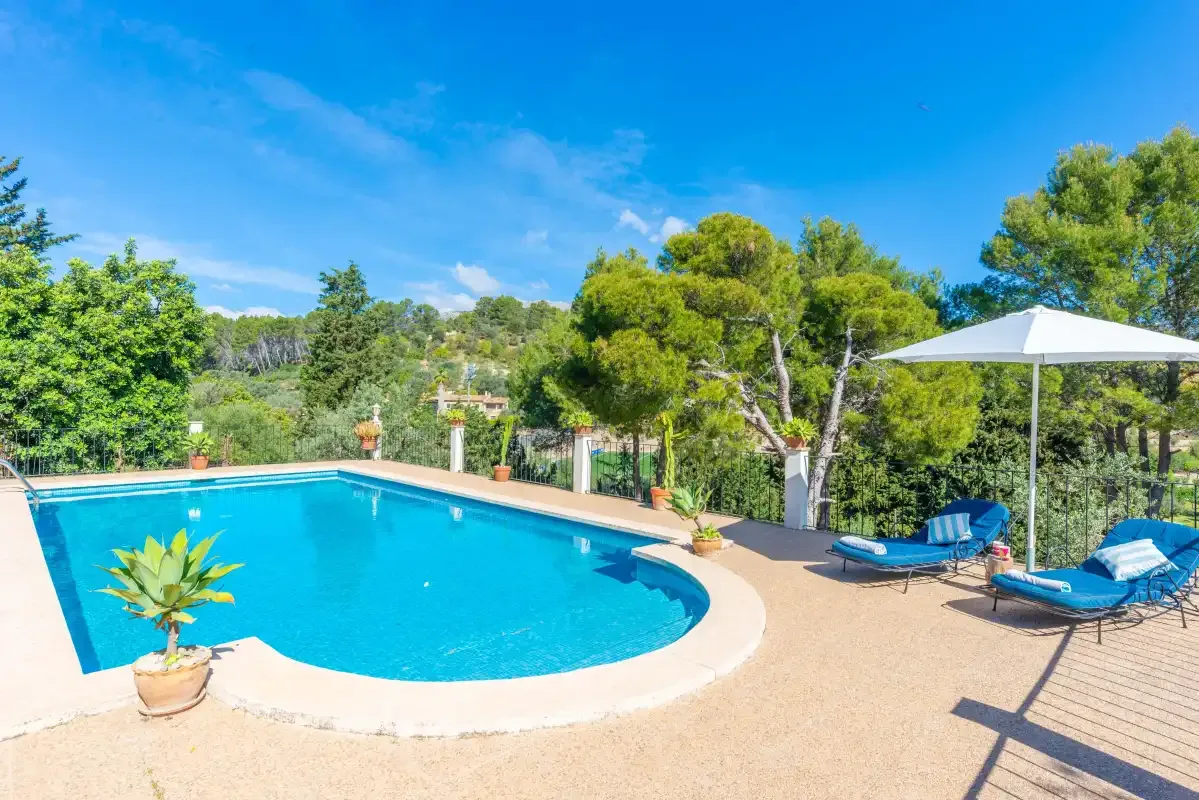 An outdoor swimming pool sits beside sun loungers and a white umbrella.