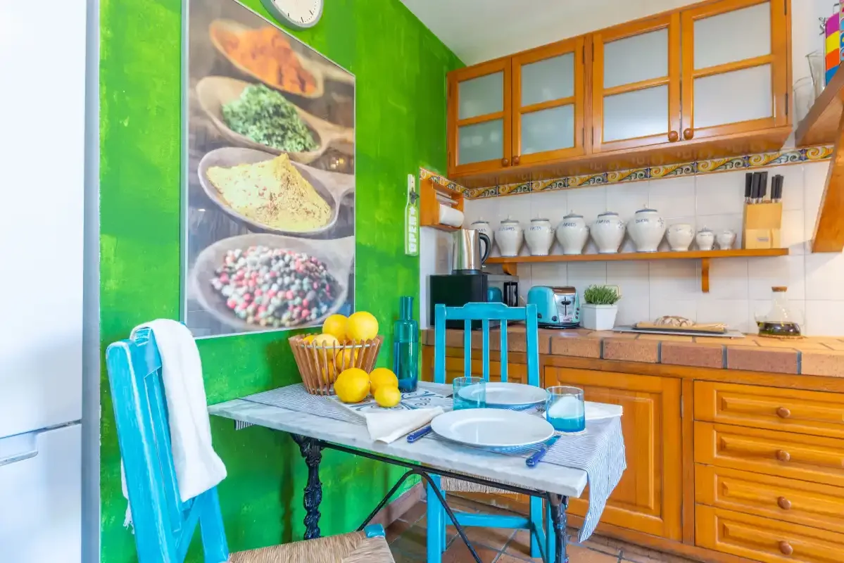 A colorful kitchen with a dining table, wooden cabinets, and countertop dishes.