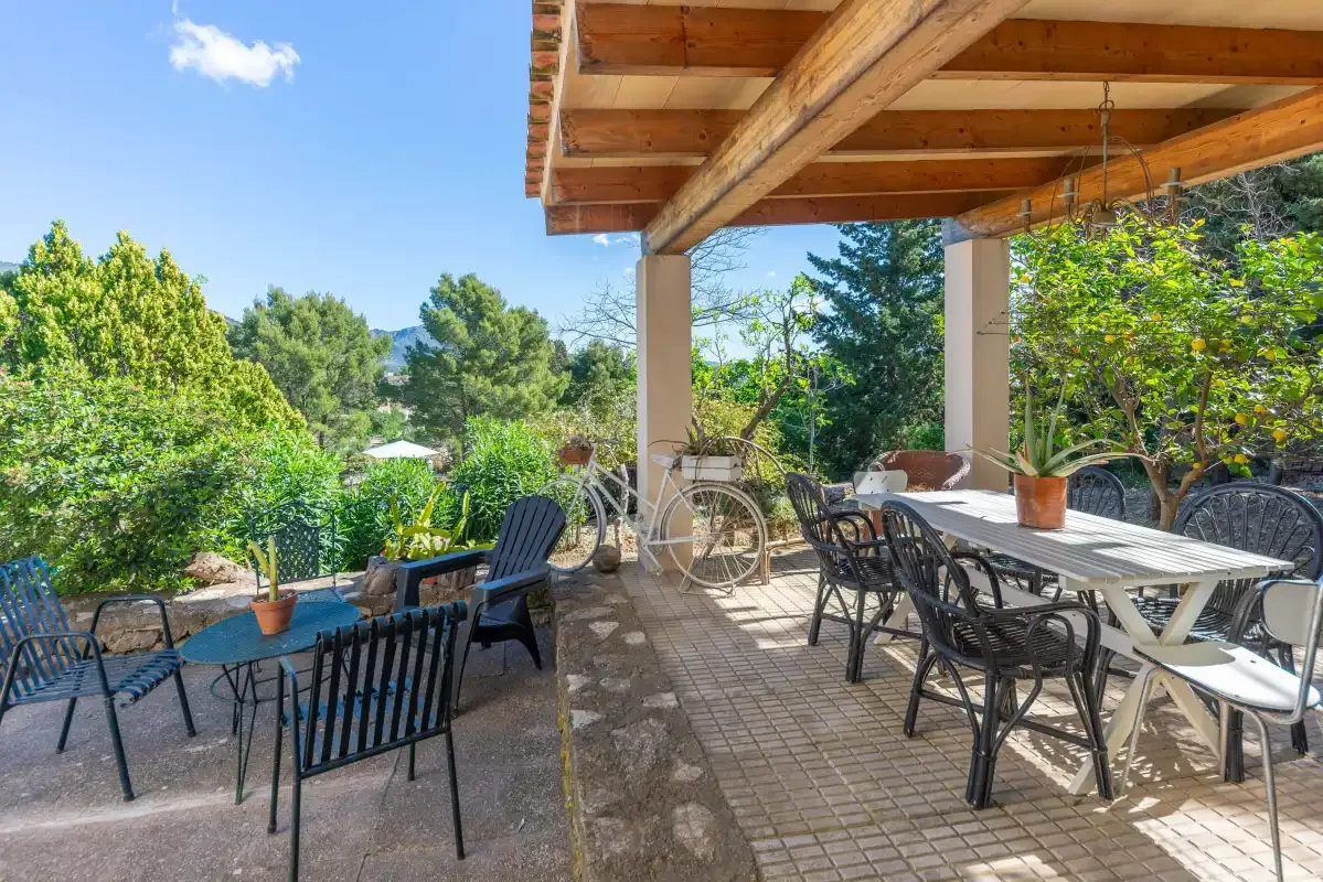 A shaded outdoor dining area with tables and seating overlooks a green garden.