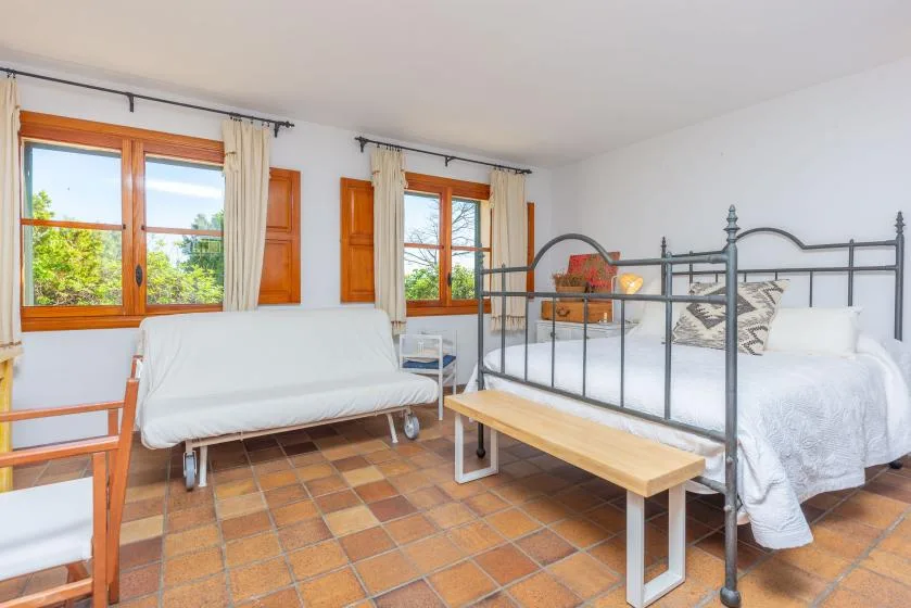 A bright bedroom with a metal bed, a sofa, and large windows.