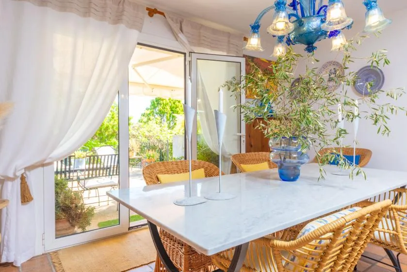 A bright dining area with a table and wicker seating beside open glass doors.