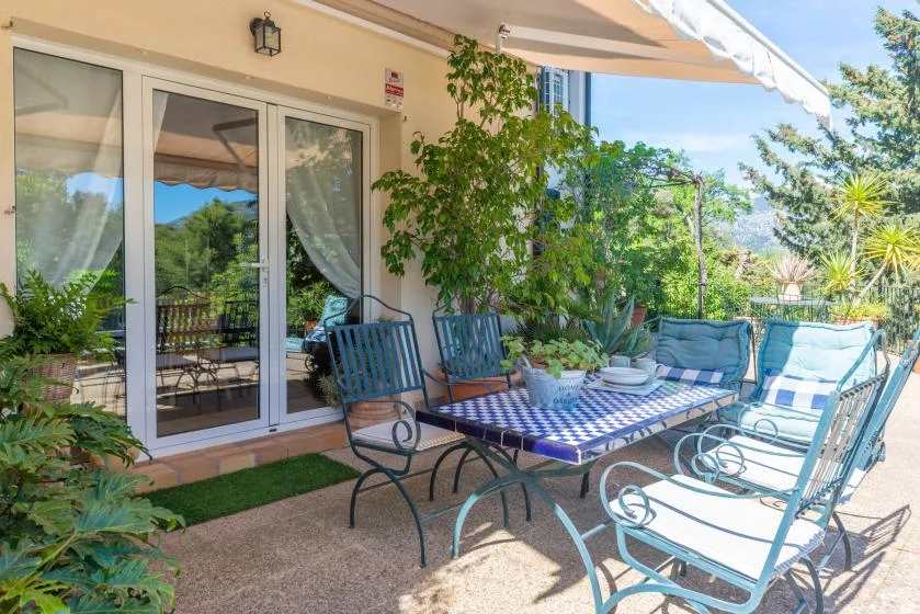 Un patio luminoso tiene asientos de metal y una mesa baja junto a puertas de vidrio.