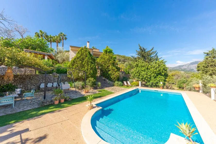 An outdoor swimming pool beside landscaped gardens and a stone retaining wall.