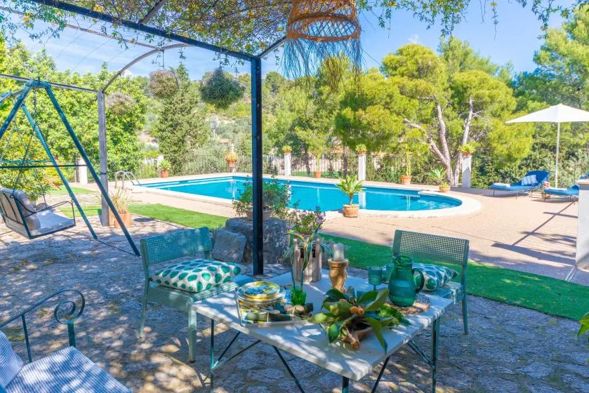 A shaded patio seating area overlooks a swimming pool and garden.