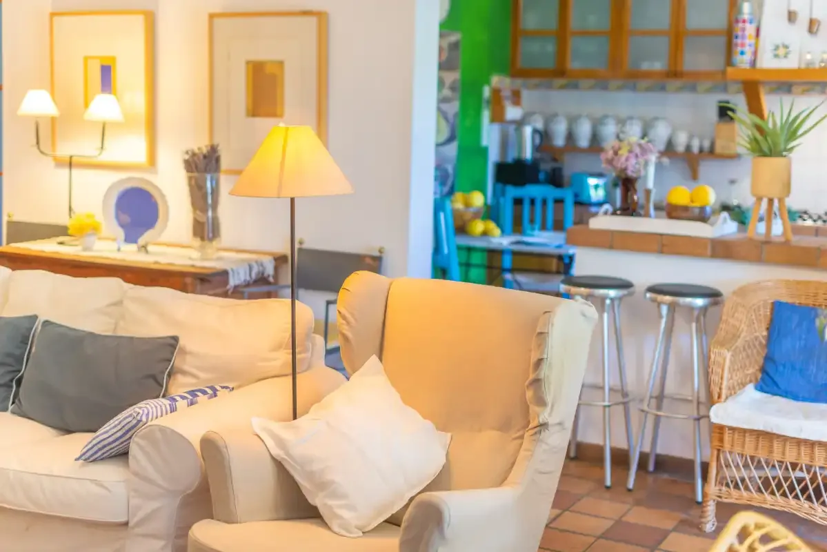 A bright living area with upholstered seating faces an open kitchen and counter.