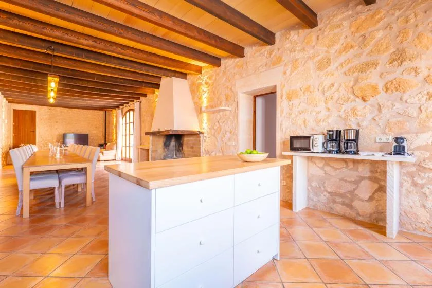 Una cocina rústica con una isla blanca, vigas expuestas y paredes de piedra.