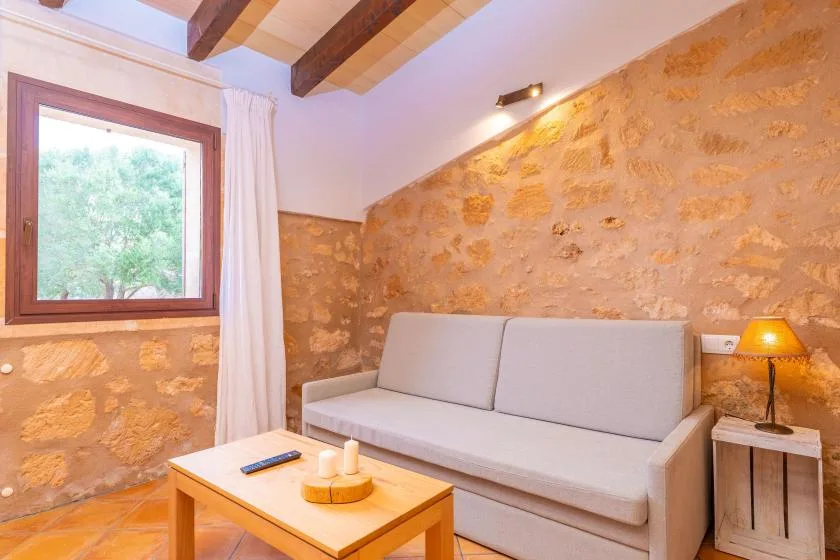 Una zona de estar con sofá claro, mesa de centro de madera y paredes de piedra.