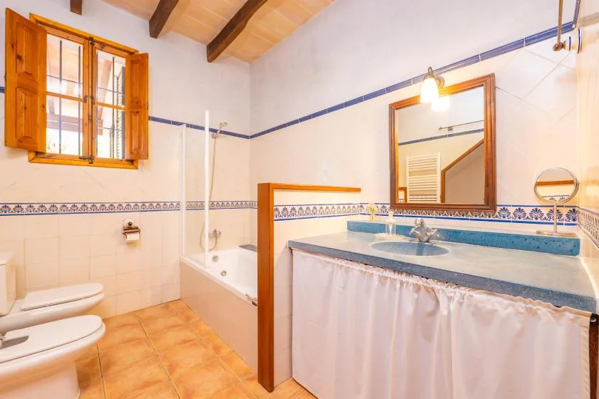 Un baño alicatado con bañera, inodoro y lavabo bajo un techo inclinado.