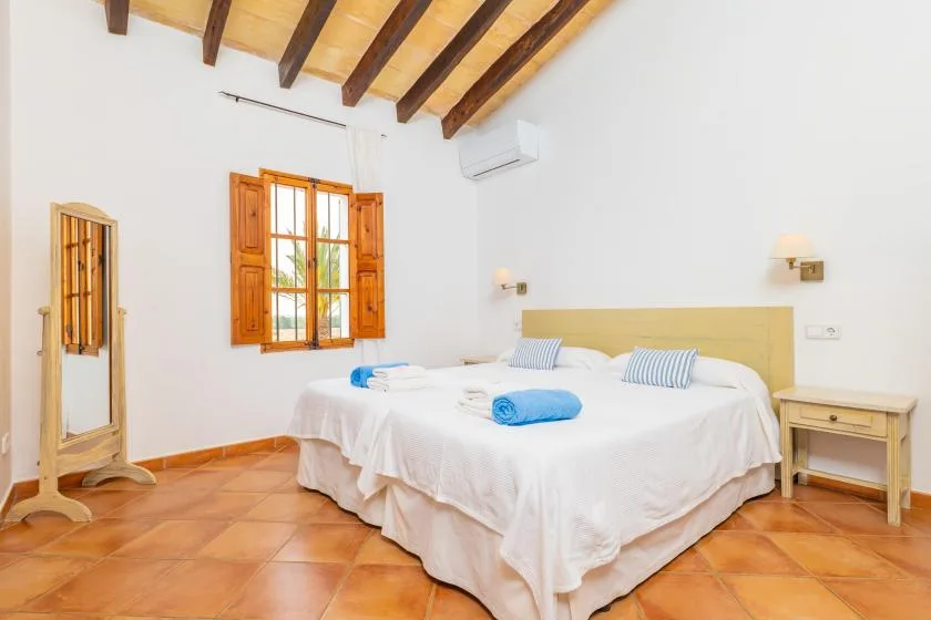 Un dormitorio luminoso con una cama grande bajo vigas de madera a la vista.