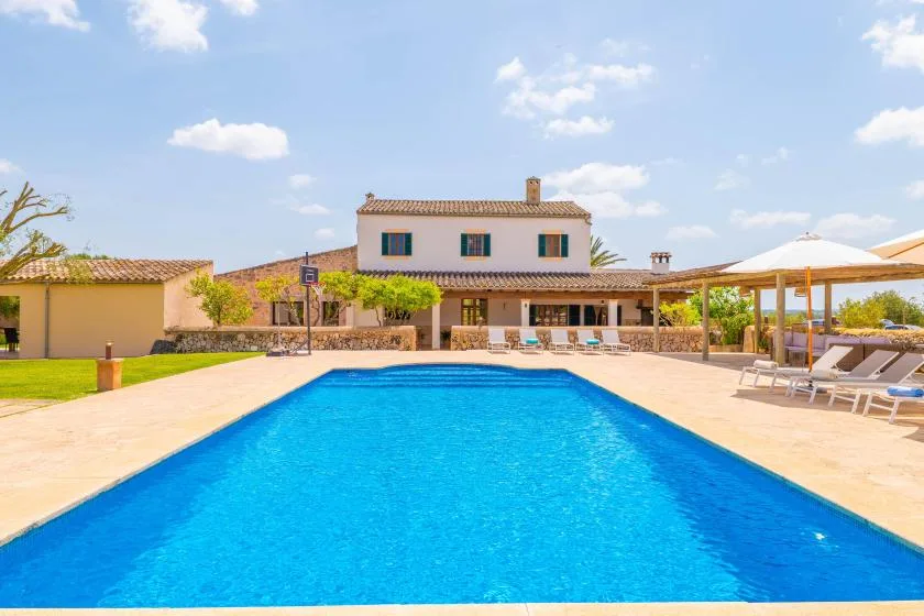 An outdoor swimming pool in front of a house, with shaded seating nearby.