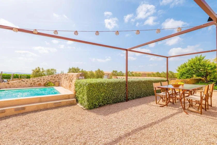 Un patio al aire libre con una pequeña piscina, mesa de comedor y pérgola.