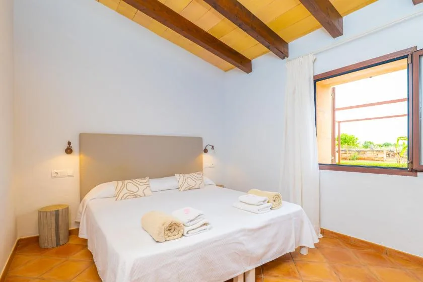 Un dormitorio luminoso con una cama bien tendida bajo vigas vistas en el techo.