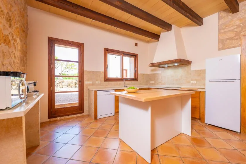 Una cocina con una isla central, vigas de madera en el techo y suelo de baldosas.
