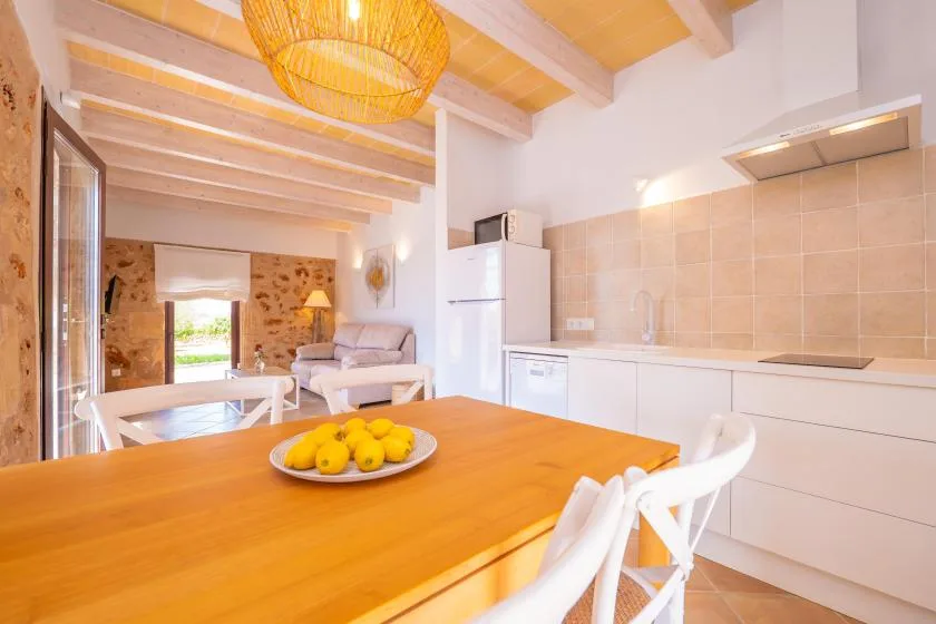 Una cocina y comedor luminosos con una mesa de madera y armarios blancos.