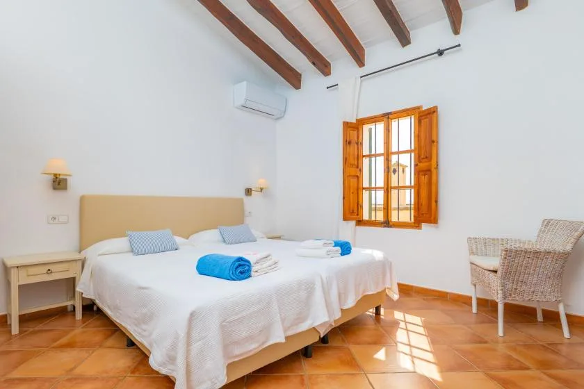 Un dormitorio luminoso con una cama doble, vigas de madera y una ventana con contraventanas.