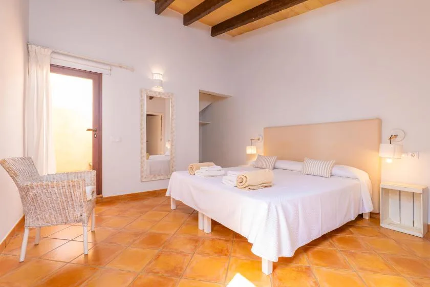 Un dormitorio con una cama, asiento de mimbre y vigas de madera a la vista.