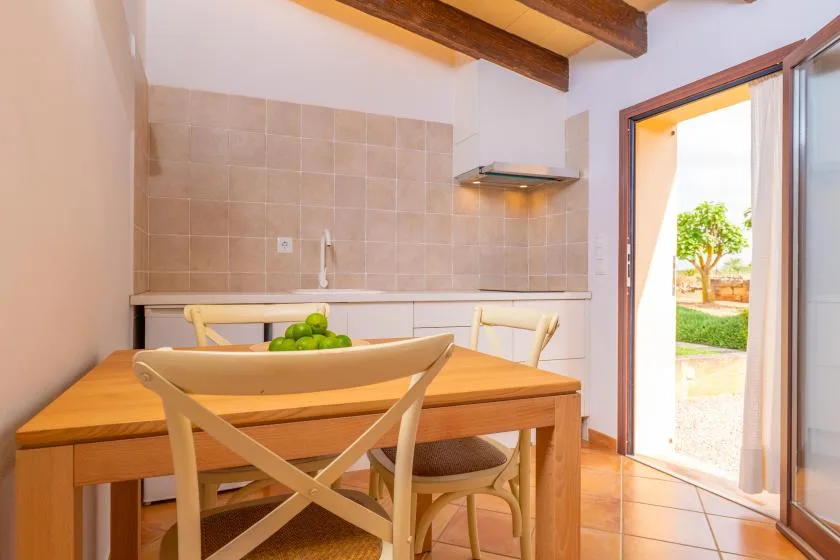 Comedor con mesa de madera junto a una cocina compacta y una puerta abierta.