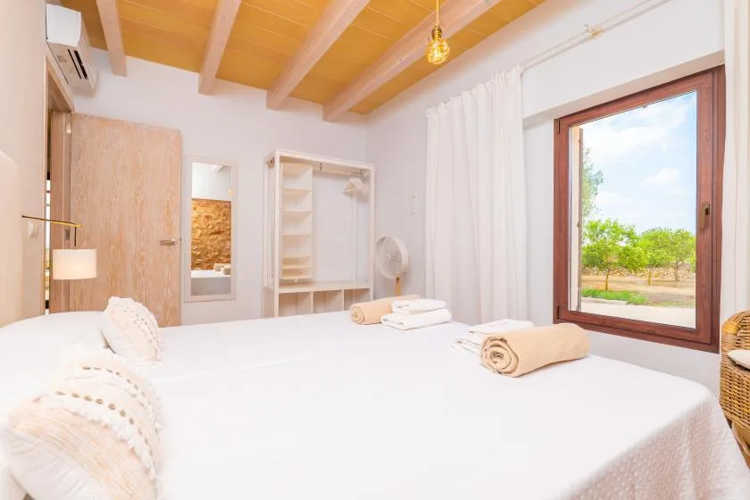 Un dormitorio luminoso con ropa de cama blanca, vigas de madera y una ventana grande.