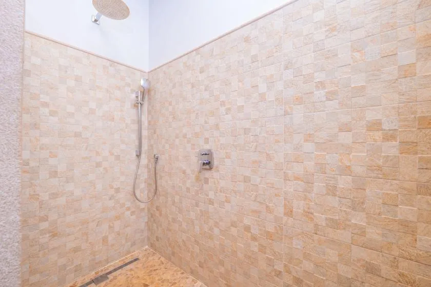 Una zona de ducha con azulejos, ducha de mano y controles en la pared.