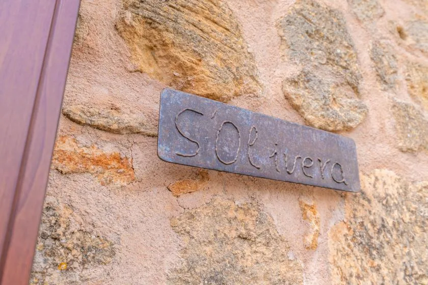 Un letrero metálico está fijado a un muro de piedra junto a un marco de madera.