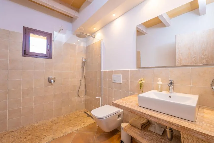 Un baño alicatado con ducha, inodoro y lavabo bajo un espejo grande.