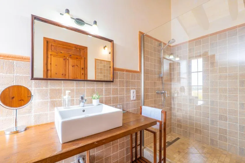 Un baño alicatado tiene un tocador de madera con lavabo blanco sobre encimera y una ducha de cristal.