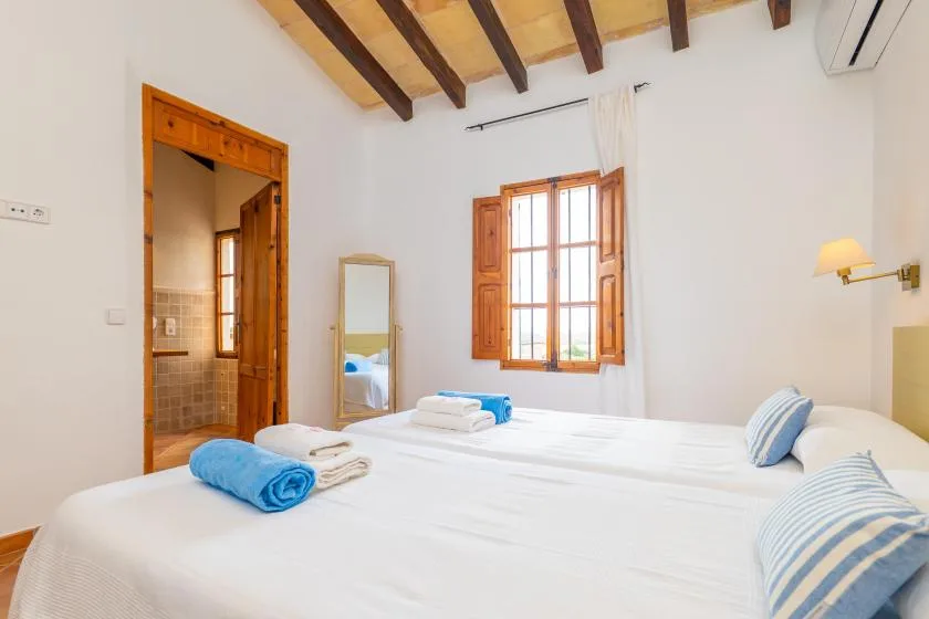 Un dormitorio luminoso con una cama blanca, una ventana de madera y vigas vistas.